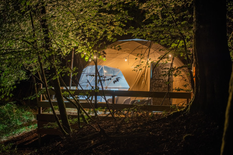 Alloggio di glamping di lusso nel bosco di notte a Glamping Auvergne-Rhone-Alpes con tenda illuminata.