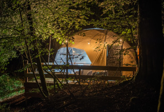 Alloggio di glamping di lusso nel bosco di notte a Glamping Auvergne-Rhone-Alpes con tenda illuminata.