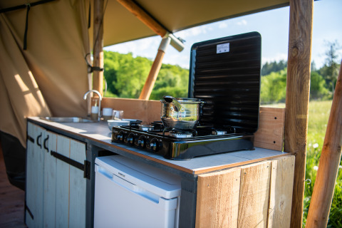 Cocina exterior en tienda glamping con estufa de gas, olla, fregadero y vista al campo en Auvernia.