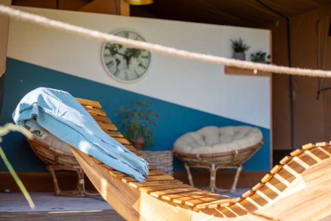Cozy glamping interior with wooden lounger, blue towel, clock, and chairs at Glamping Auvergne-Rhone-Alpes.