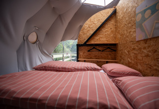 Innenansicht eines Glampingzelts in Auvergne-Rhone-Alpes mit Doppelbett, Holzdekor und Fenster.