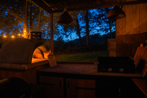 Cucina all'aperto al tramonto con forno per pizza, barbecue e luci a Glamping Auvergne, Auvergne-Rhone-Alpes.