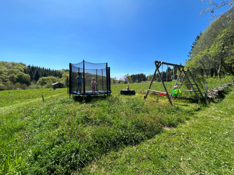 Children playing on a trampoline and swingset in a lush field at Glamping Auvergne under a clear blue sky.