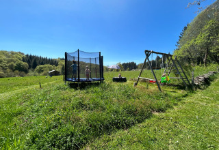 Niños jugando en una cama elástica y columpios en un campo verde en Glamping Auvergne bajo el cielo azul.