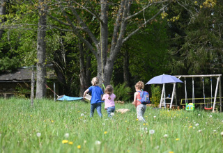 Des enfants jouent dans une prairie près de tentes glamping et de balançoires à Glamping Auvergne, Auvergne-Rhône-Alpes.