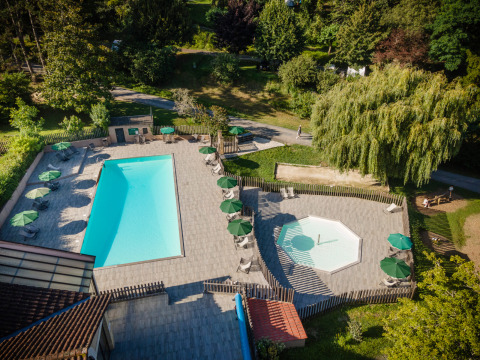Aerial view of pools and loungers at Huttopia Sarlat - Glamping Dordogne surrounded by greenery and trees.