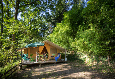 Glamping indkvartering ved Huttopia Sarlat - Glamping Dordogne, omgivet af grønne træer og natur, folk slapper af foran telt.