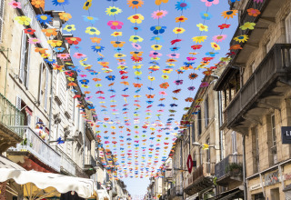 Colorful flowers strung above a lively street market near Huttopia Sarlat - Glamping Dordogne, Dordogne, France.