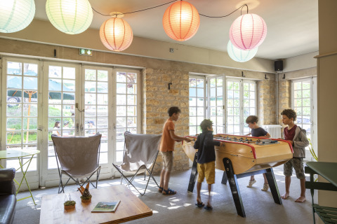 Des enfants jouent au baby-foot dans le salon commun à Huttopia Sarlat - Glamping Dordogne.