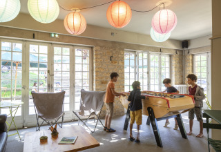 Des enfants jouent au baby-foot dans le salon commun à Huttopia Sarlat - Glamping Dordogne.