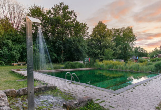 Naturlig swimmingpool og udendørs bruser ved solnedgang på Uhlenköper-Camp Uelzen, glamping i Niedersachsen.