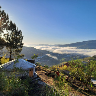 Alojamiento glamping en Quinta das Corujeiras entre colinas y árboles, con niebla matutina en el valle.