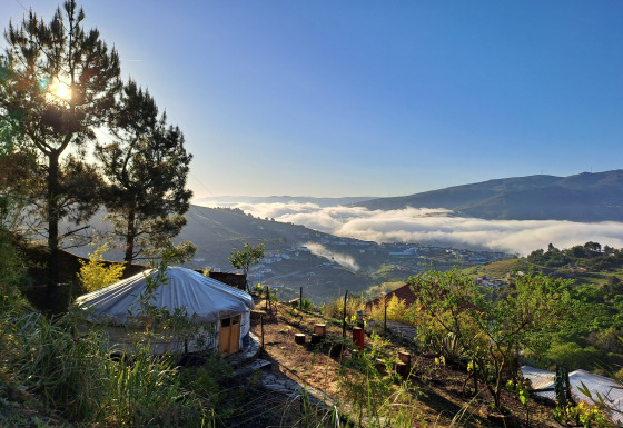 Alojamiento glamping en Quinta das Corujeiras entre colinas y árboles, con niebla matutina en el valle.