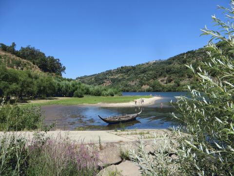 Vista sul fiume con barca e colline verdi al glamping Quinta das Corujeiras in Portogallo.
