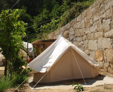 Alloggio glamping in tenda accanto a un muro di pietra a Quinta das Corujeiras, circondato dal verde.