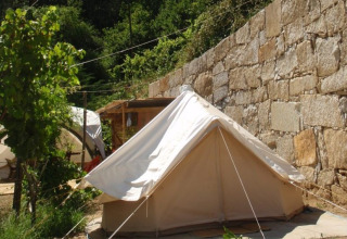 Alojamiento de glamping en una tienda junto a un muro de piedra en Quinta das Corujeiras, rodeada de vegetación.