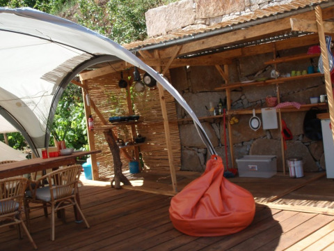 Outdoor glamping kitchen and lounge area with wooden furniture and orange bean bag at Quinta das Corujeiras.