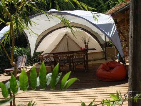 Glamping alla Quinta das Corujeiras con tenda, terrazza in legno, sedie e pouf immersi nella natura.