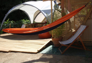 Espacio al aire libre en Quinta das Corujeiras glamping con hamaca naranja y silla plegable junto a una carpa.
