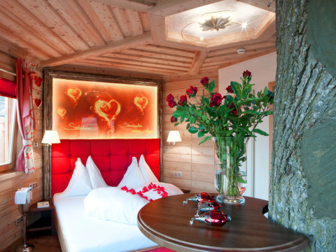 Habitación glamping romántica en Baumhaus Hotel Prechtlhof con tronco de árbol, cama doble y rosas.