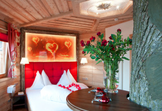 Romantische glampingkamer in Baumhaus Hotel Prechtlhof met boomstam, tweepersoonsbed en rozenboeket.