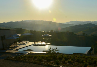 Udsigt over Brezza di sera agriturismo glampingtelte med infinity pool og bjerge i solnedgang.