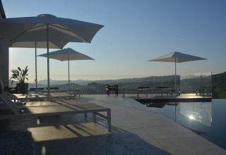 Luxury sun loungers and umbrellas by the infinity pool overlooking hills at Brezza di sera Glamping tents.