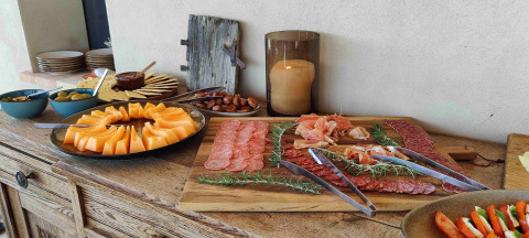 Buffet con melón, embutidos, aceitunas y aperitivos en mesa rústica en Brezza di sera agriturismo Glampingtenten Le Marche.
