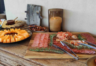 Buffet con melone, salumi, olive e antipasti su tavolo rustico presso Brezza di sera agriturismo Glampingtenten Le Marche.