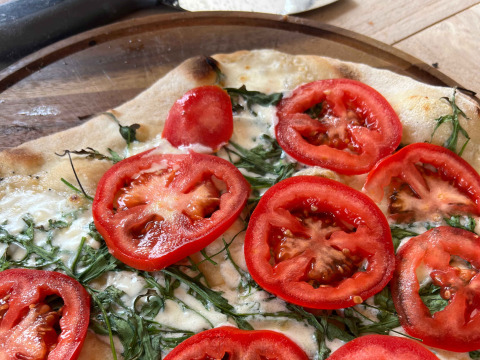 Freshly baked pizza with sliced tomatoes, arugula, and cheese served at Brezza di sera agriturismo Glampingtenten Le Marche.
