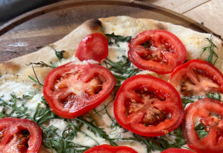 Frisklavet pizza med frisk tomat, rucola og mozzarella på træfad under ophold på Brezza di sera agriturismo Glampingtenten Le Marche.