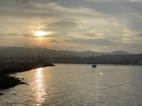 Atardecer sobre el agua en Brezza di sera agriturismo - Glampingtenten Le Marche, con barco y colinas.