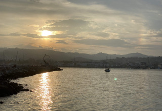 Sunset over the water at Brezza di sera agriturismo - Glampingtenten Le Marche, with a boat and hills in view.