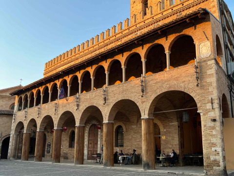 Historic brick building with arches and terrace lit by sunset, typical of Le Marche region in Italy.