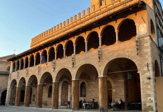 Historic brick building with arches and terrace lit by sunset, typical of Le Marche region in Italy.