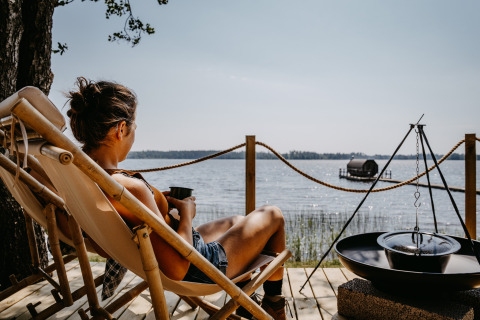 Persoon ontspant in een stoel bij Nordic Woods Wildernis Glamping Zweden met uitzicht op het meer.