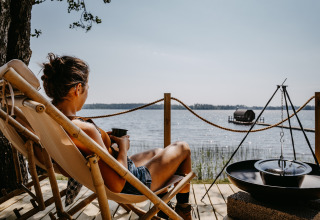 Persoon ontspant in een stoel bij Nordic Woods Wildernis Glamping Zweden met uitzicht op het meer.