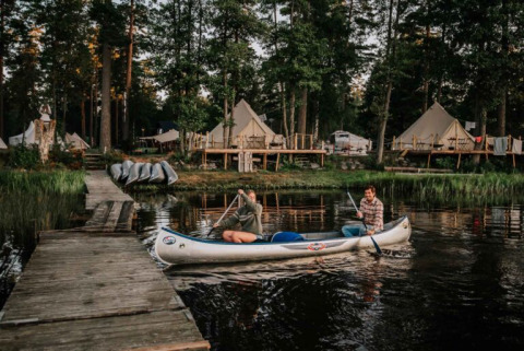 Twee mensen kanoën bij een steiger met glampingtenten in het bos bij Nordic Woods - Wildernis Glamping Zweden.