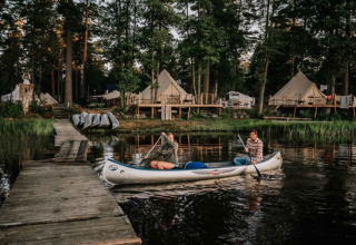 Twee mensen kanoën bij een steiger met glampingtenten in het bos bij Nordic Woods - Wildernis Glamping Zweden.