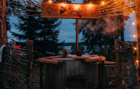 Twee mensen ontspannen samen in een houten hottub bij Nordic Woods Wildernis Glamping Zweden in de avond.