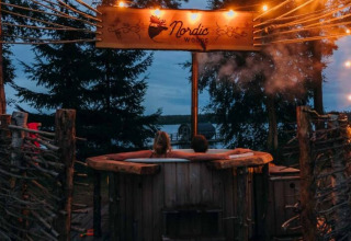 Twee mensen ontspannen samen in een houten hottub bij Nordic Woods Wildernis Glamping Zweden in de avond.