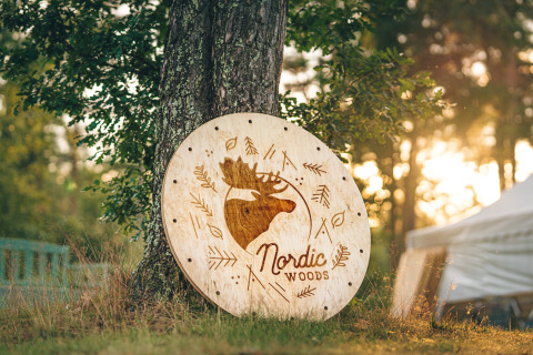 Houten bord met het logo 'Nordic Woods' bij een boom, glamping accommodatie in Zweden bij zonsondergang.