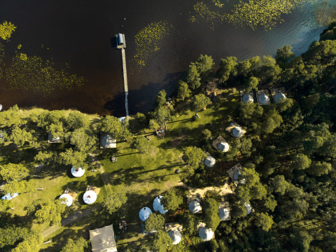 Luchtfoto van Nordic Woods Wildernis Glamping Zweden met tenten aan een meer en omringd door bos.