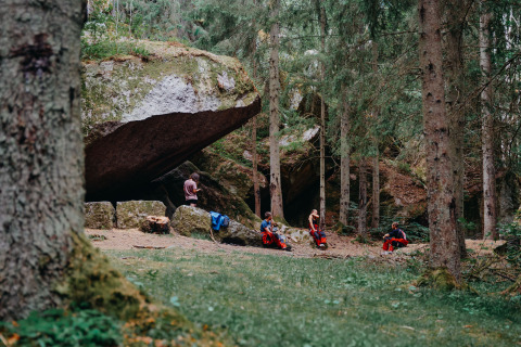 Nordic Woods Wildernis Glamping Zweden met mensen relaxend bij grote stenen in het bos en de natuur.