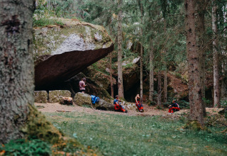 Nordic Woods Wildernis Glamping Zweden met mensen relaxend bij grote stenen in het bos en de natuur.