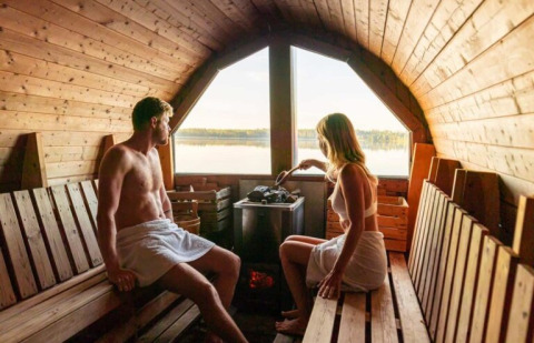Twee personen ontspannen in een houten sauna met uitzicht op het meer bij Nordic Woods - Wildernis Glamping Zweden.