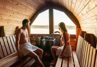Twee personen ontspannen in een houten sauna met uitzicht op het meer bij Nordic Woods - Wildernis Glamping Zweden.