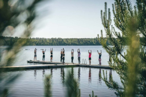 Groep mensen doet samen yoga op een steiger aan een meer bij Nordic Woods - Wildernis Glamping Zweden.