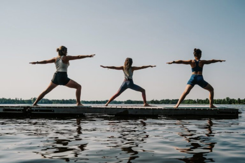 Drie mensen doen yoga op een steiger bij het meer bij Nordic Woods - Wildernis Glamping Zweden accommodatie.