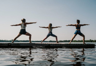 Drie mensen doen yoga op een steiger bij het meer bij Nordic Woods - Wildernis Glamping Zweden accommodatie.